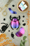 Colorful rainbow paper scarab beetle craft made with folded paper by Assembli, showcasing vibrant, intricate craft details.
