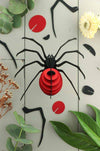 Red paper spider craft made from Assembli Paper Spider kit, showcasing detailed paper legs and body for creative arts projects.