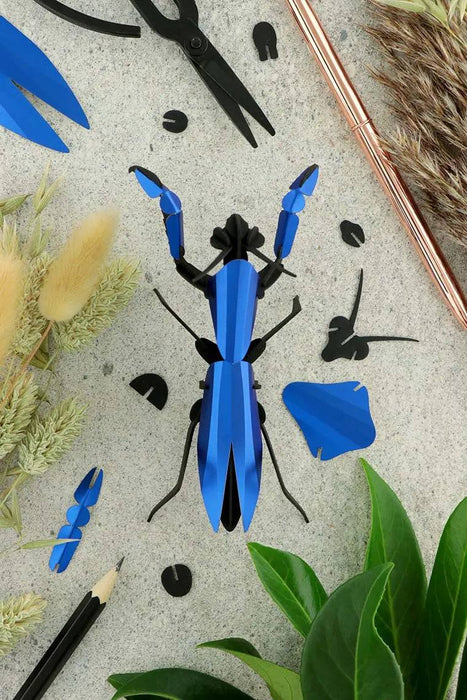 Red metal paper praying mantis craft by Assembli, featuring detailed wings and body made from textured paper material.