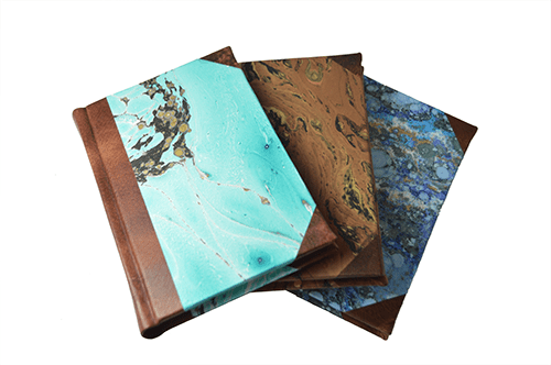 Handcrafted leather-trimmed journal with marbled paper pages and modern spine, featuring small lined pages in turquoise by Il Cartiglio.