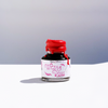 Papier Plume New Orleans Collection fountain pen ink bottle with vibrant ink inside, displayed alongside colorful feather boas.